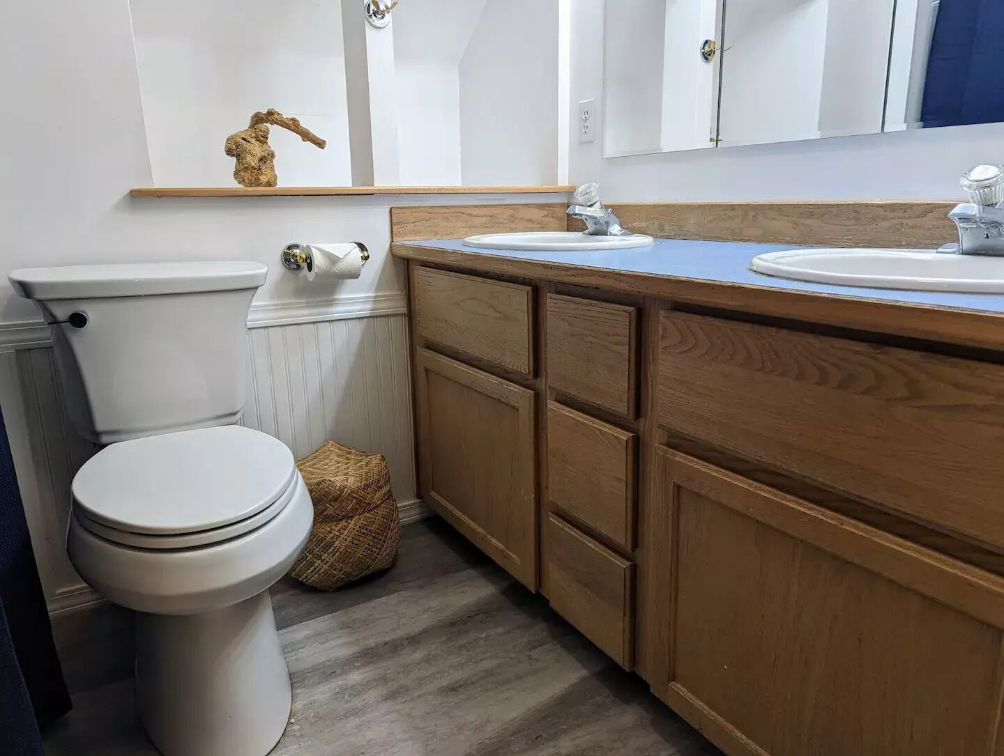 A bathroom with a white toilet, wooden cabinets, a sink, and a mirror.