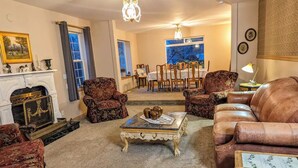 A traditional living room with a fireplace, ornate armchairs, a leather sofa, and a dining area with a table and chairs. - Alegria!  Five Bedroom Colonial Style Home Conveniently Located! Pet Friendly! (Moses Lake)
