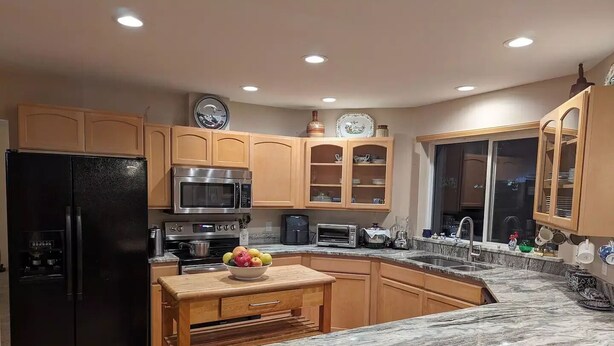 A modern kitchen with wooden cabinets, a black refrigerator, a microwave, a stove, and a marble countertop. - Alegria!  Five Bedroom Colonial Style Home Conveniently Located! Pet Friendly! (Moses Lake)