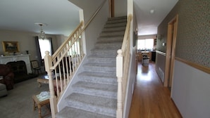 A staircase with wooden railings and carpeted steps leading to a second floor. A dining area with a table and chairs is visible in the background. - Alegria!  Five Bedroom Colonial Style Home Conveniently Located! Pet Friendly! (Moses Lake)