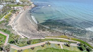 Vista aérea de una zona costera con playa, costa rocosa y un parque con senderos y vegetación.