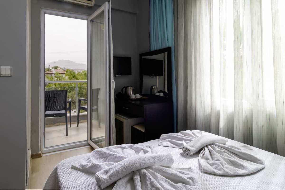 A hotel room with a bed, a desk with a chair, a television, and a view of greenery outside.