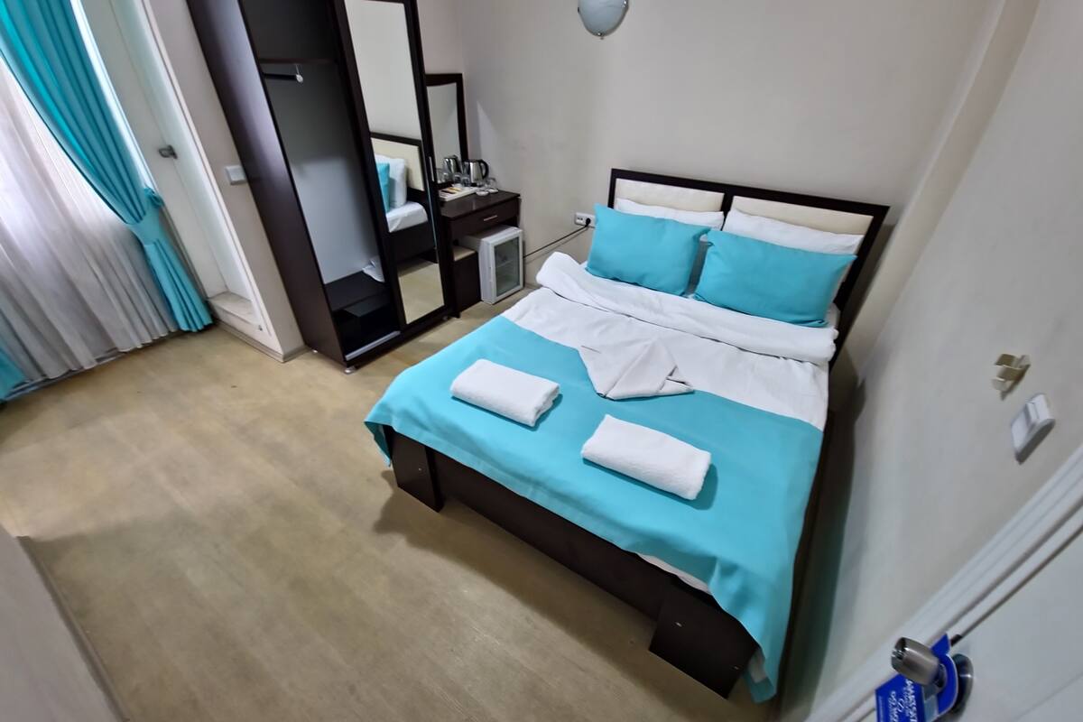 A hotel room with a bed, a bedside table, a mirror, and a wardrobe.