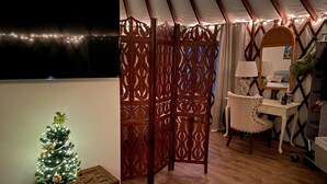 Ein gemütliches Zimmer mit Holzboden, einem kleinen Weihnachtsbaum, einem Fernseher, einem Schreibtisch mit Lampe und einem Bett mit Baldachin.