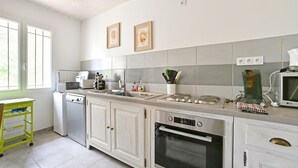 A kitchen with white cabinets, a built-in oven, a stove, and a microwave. There are two framed pictures on the wall, a window with blinds, and a yellow cart. - 2 bedroom gorgeous apartment in Codognan (Codognan)