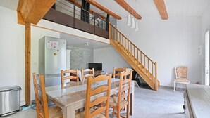 A dining area with a wooden table and chairs, a kitchen in the background, and a wooden staircase. - 2 bedroom gorgeous apartment in Codognan (Codognan)