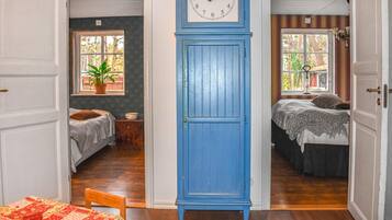A room with a large blue clock, two beds, a window with a view of trees, and a door leading to another room.