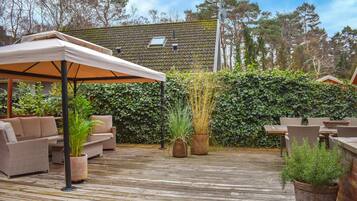 An outdoor patio with wicker furniture, a covered seating area, and potted plants.
