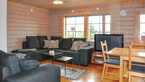 Ein gemütliches Blockhaushaus-Interieur mit einer Couch, einem kleinen Tisch, einem Fernseher und einem Holzesstisch mit Stühlen.