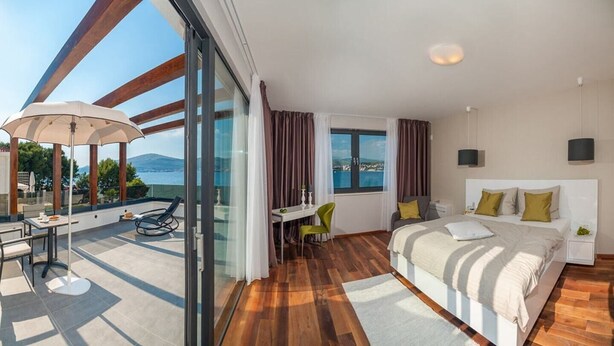A modern hotel room with a large bed, a desk with a chair, a balcony with a table and chairs, and a view of the sea. - Villa Safranka - Private villa with pool (Okrug Gornji)