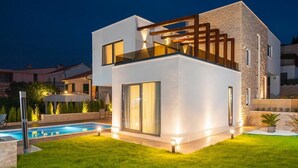 A modern two-story house with a swimming pool, large windows, and a well-lit exterior. - Villa Safranka - Private villa with pool (Okrug Gornji)