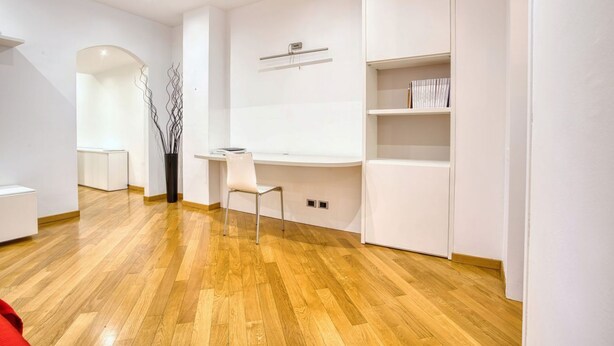 A modern, minimalist room with a wooden floor, white walls, a desk with a chair, and built-in shelving.