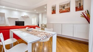 A modern living room with a red sofa, white dining table, and chairs, a TV, and artwork on the walls.
