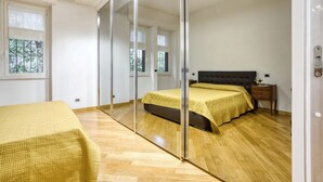 A bedroom with a bed, a bedside table, a mirror, and a window.