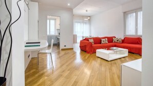 A spacious living area with a red sofa, a white coffee table, and a dining area with a white table and chairs.