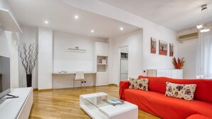 A modern living room with a red sofa, a glass coffee table, and a white TV stand.