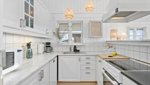 Una cocina moderna con armarios blancos, horno empotrado, microondas, cafetera y lavaplatos.