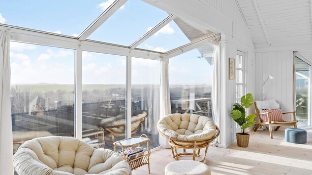 Una habitación amplia con ventanas grandes, mobiliario de mimbre y vistas al campo.