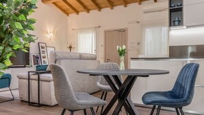 Uma sala de estar moderna com uma mesa redonda, duas cadeiras cinzas, uma cadeira azul, um sofá e um vaso com planta.