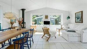 A spacious living area with a wooden dining table, blue chairs, a white sofa, and a TV mounted on the wall.