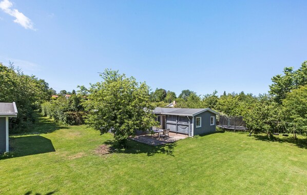 Une cour arrière d’une maison, avec un petit chalet, un trampoline et un arbre.
