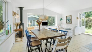 A spacious dining area with a large wooden table and chairs, a built-in stove, and large windows offering a view of the outdoors.