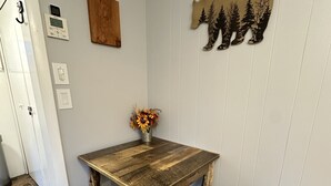 Un coin repas avec une table et des bancs en bois rustique, un vase rempli de fleurs séchées et une décoration murale représentant des arbres.