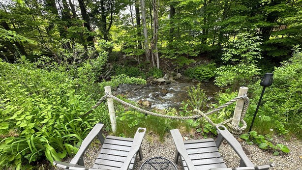 Un banc et une table en bois sont installés près d’un ruisseau, dans une zone boisée.