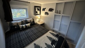 Une chambre à coucher comprenant un lit, une table de chevet, une lampe, une fenêtre avec des rideaux, un mur décoré de tableaux encadrés et des étagères intégrées.