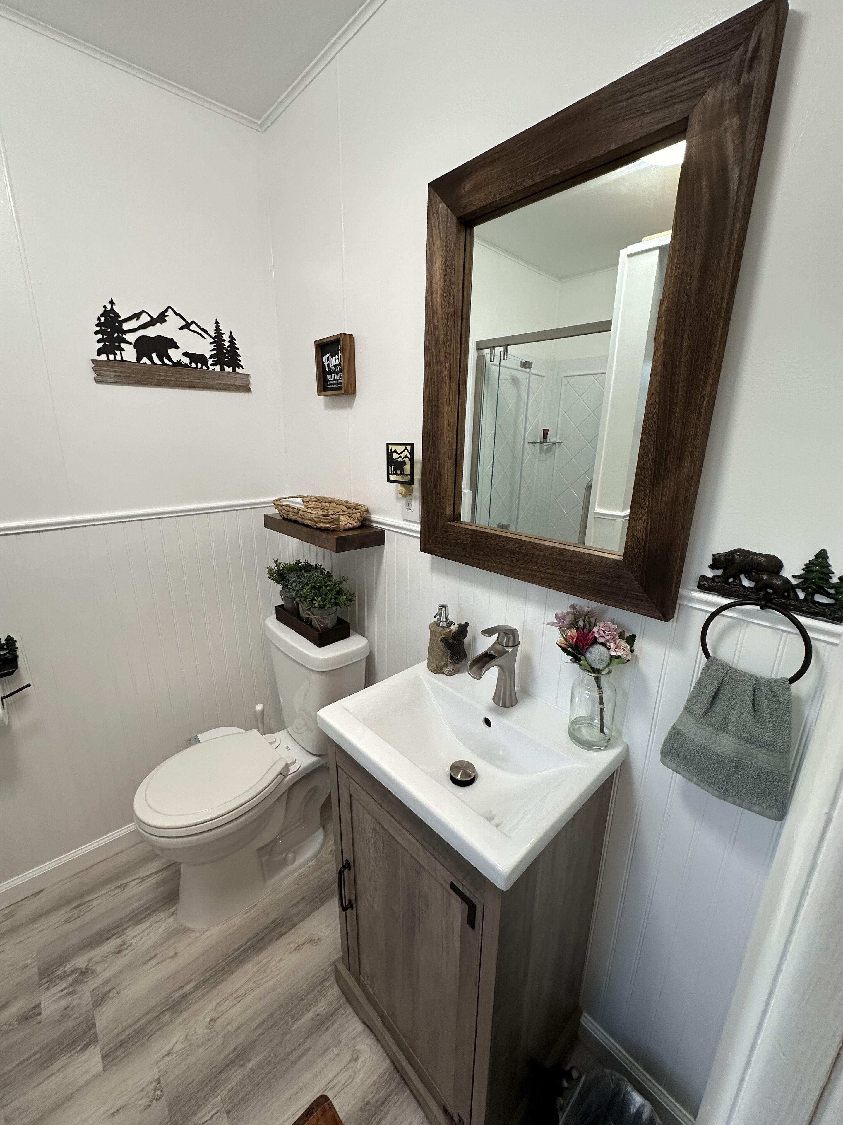 Ein Badezimmer mit Toilette, einem Waschbecken mit Holdekor, einem Spiegel mit Holzrahmen und einer Duschkabine.