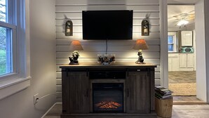 Un salon doté d’une cheminée, d’un téléviseur fixé au mur et de deux lampes posées sur une console en bois.