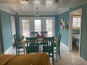 A dining area with a table and chairs, a view of the outside, and a bed in the adjacent room.