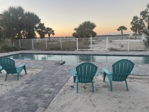 A pool area with three green chairs, a paved walkway, and a fence.