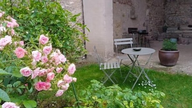 A garden area with a table and chairs, surrounded by lush greenery and flowering plants. - Les Peupliers - Poilly (Poilly)