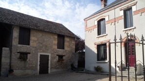 A courtyard with stone buildings, a gravel ground, and a metal gate. - Les Peupliers - Poilly (Poilly)