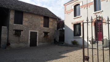 Une cour bordée de bâtiments en pierre, avec un sol recouvert de gravier et une porte en métal.