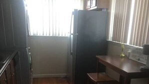 Eine kleine Küche mit Holzboden, einem Kühlschrank, einer Spüle und einem Fenster mit Jalousien.