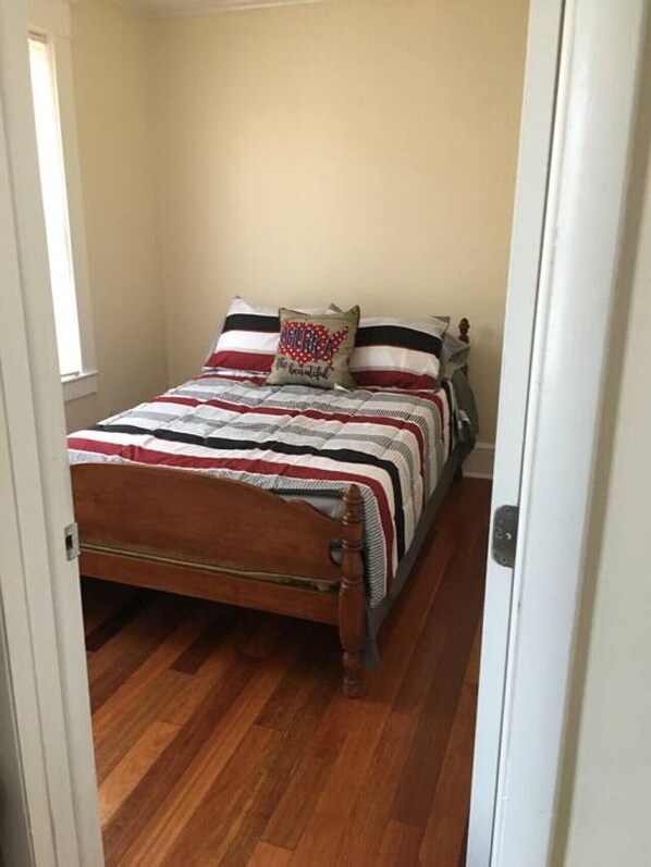 A narrow room with a wooden bed, striped bedding, and a single pillow with a red and white design.