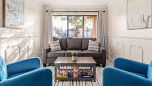A living room with a grey sofa, two blue armchairs, a coffee table with snacks, and a large window with curtains. - Urban Escape! Massive home in Central Bakersfield! (Bakersfield)