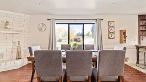 A dining area with a brick wall, a fireplace, a large window with curtains, and a sign with letters. - Urban Escape! Massive home in Central Bakersfield! (Bakersfield)