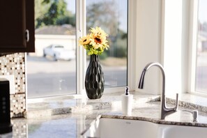 Enjoy a view of the street from this kitchen, featuring a large window, a vase with flowers, a stainless steel faucet, and a white sink.