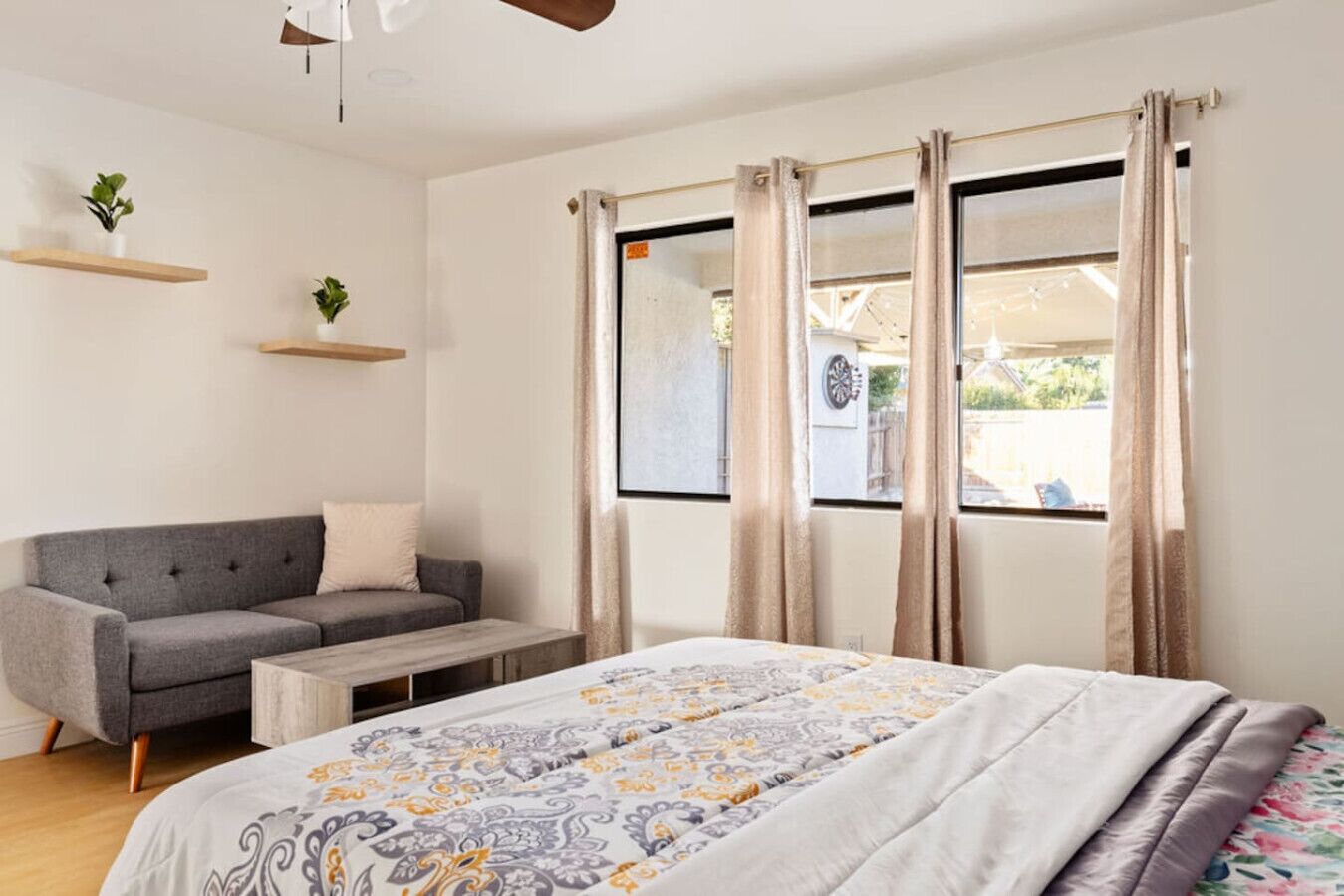 A bedroom with a bed, a grey sofa, a wooden coffee table, and a window with curtains.