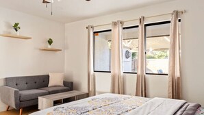 A bedroom with a bed, a grey sofa, a wooden coffee table, and a window with curtains. - Urban Escape! Massive home in Central Bakersfield! (Bakersfield)