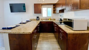 Une cuisine moderne avec des meubles de rangement en bois foncé, un plan de travail en granit, un four à micro-ondes encastré et un luminaire au plafond.