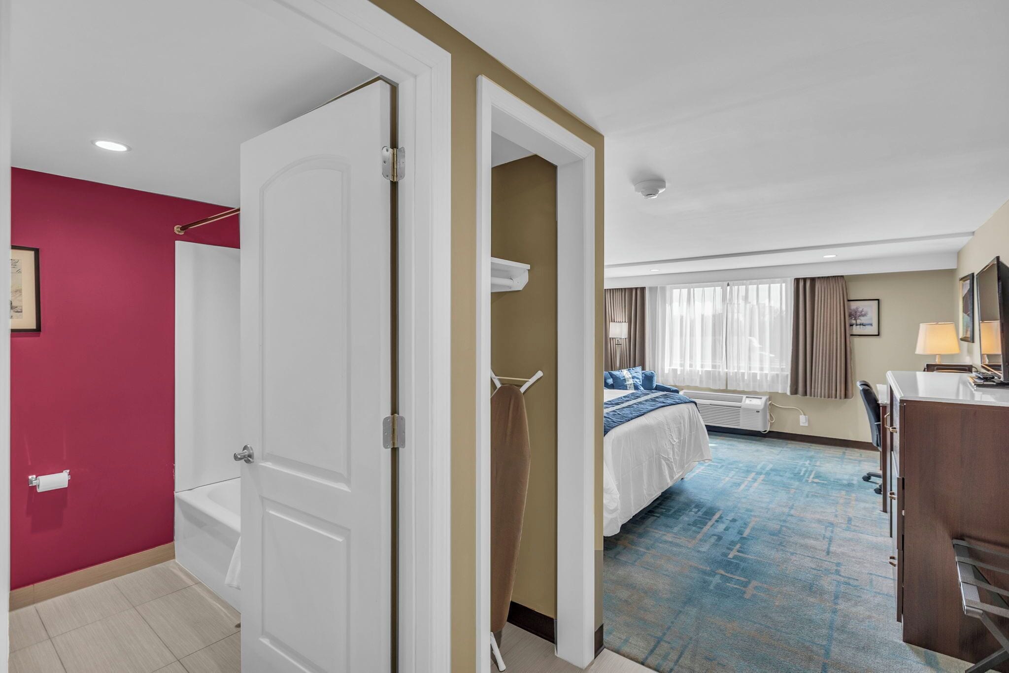 Habitación de hotel con cama, escritorio, silla, baño con bañera y ventana con cortinas.