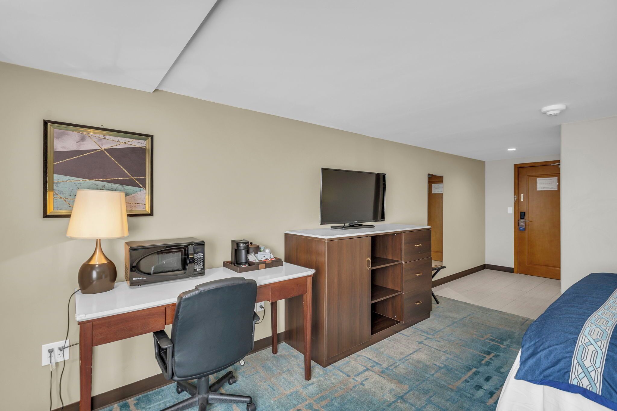 A hotel room with a desk, a television, a bed, and a door.