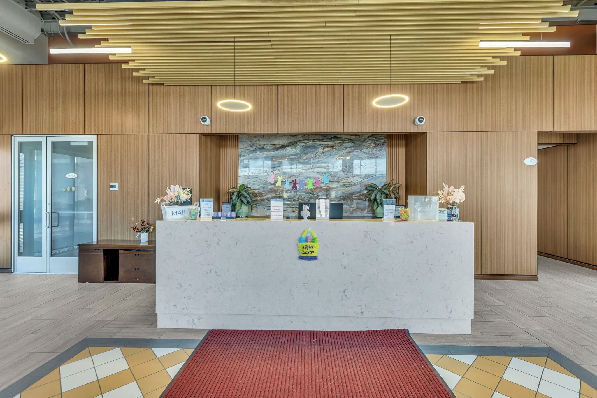 A reception desk with a marble top, wooden panel walls, and a red carpet leading to it.