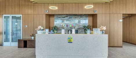 A reception desk with a marble top, wooden panel walls, and a red carpet leading to it.
