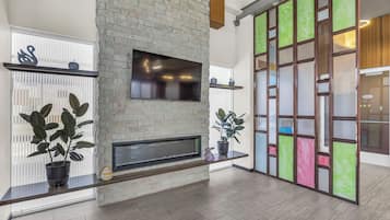 A modern living room with a stone fireplace, a flat-screen TV mounted above it, and a large window with blinds.