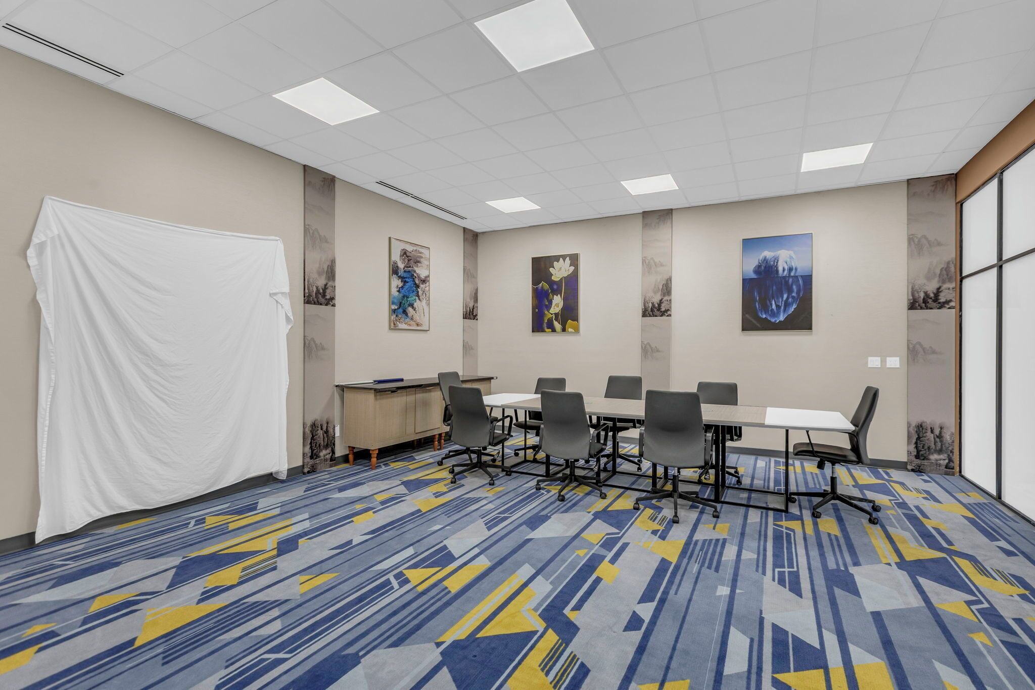 A conference room with a large table, chairs, and artwork on the walls.